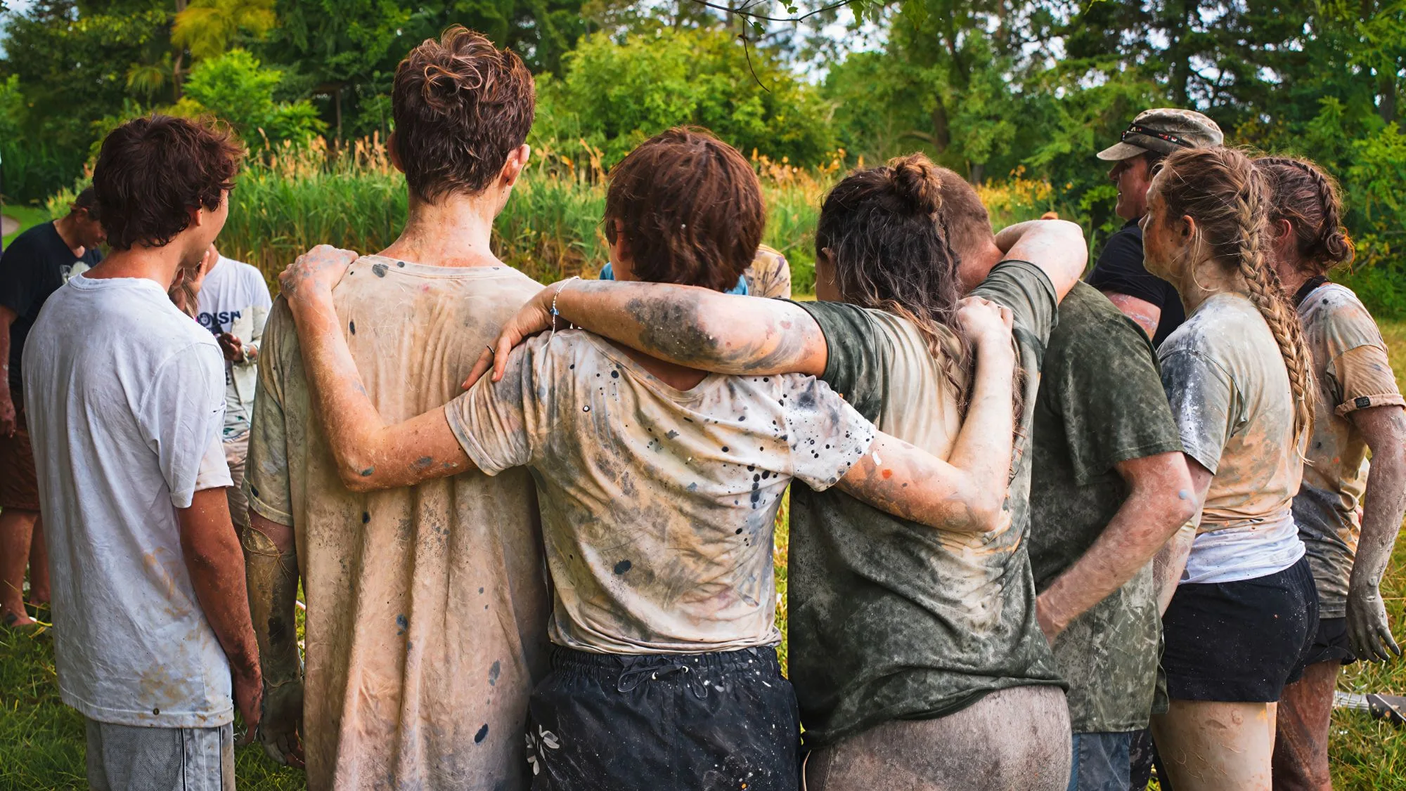 A team of colleagues covered in mud with their arms around each other after a team-building activity